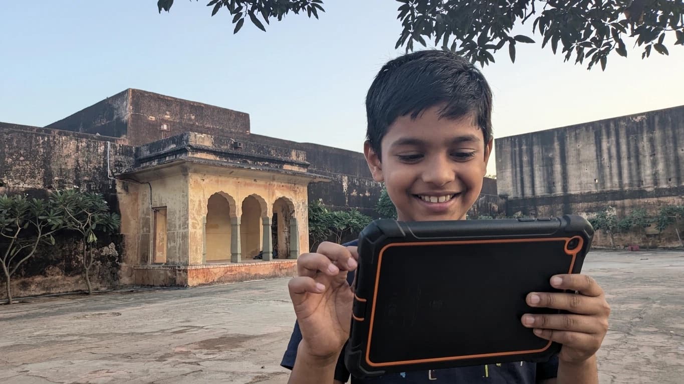 A smiling young visitor holds a tour tablet in a courtyard of Jaigarh Fort